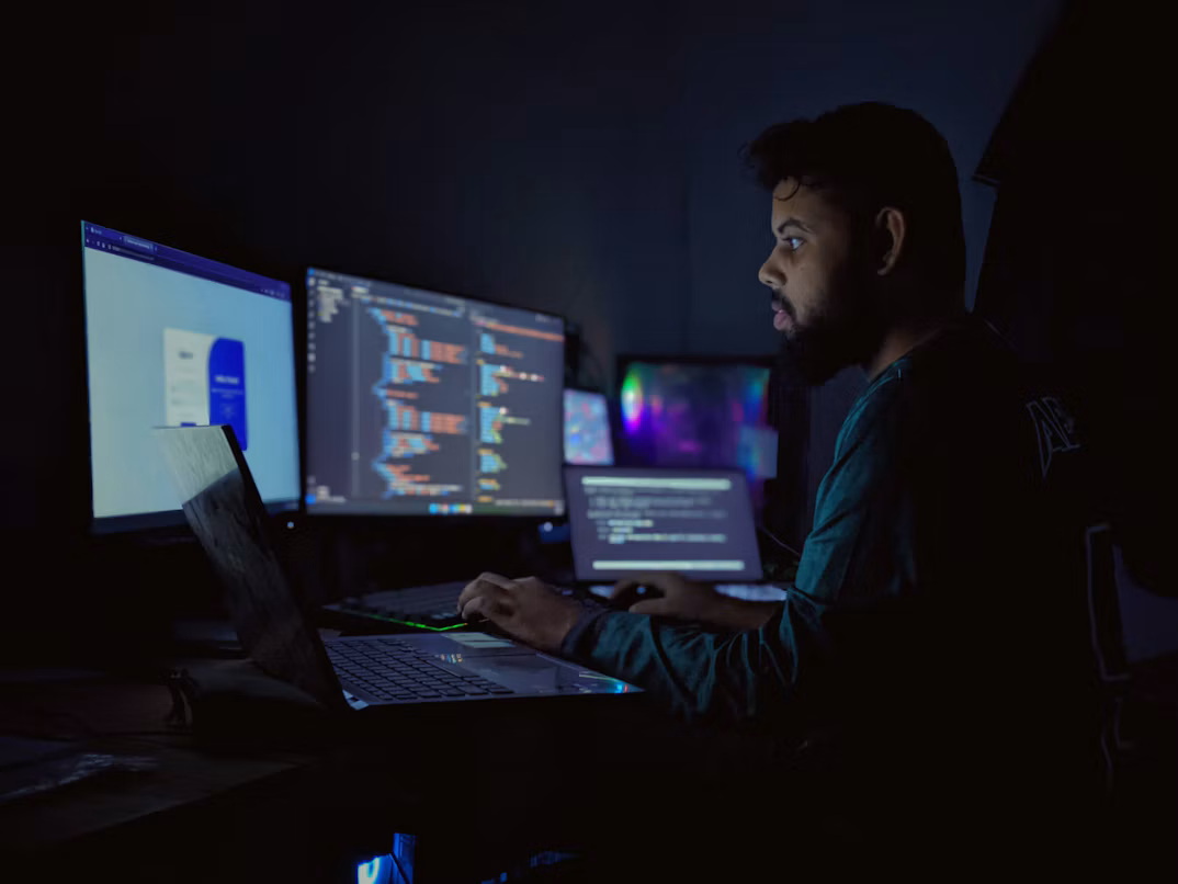 Software developer working at a laptop beside multiple monitors